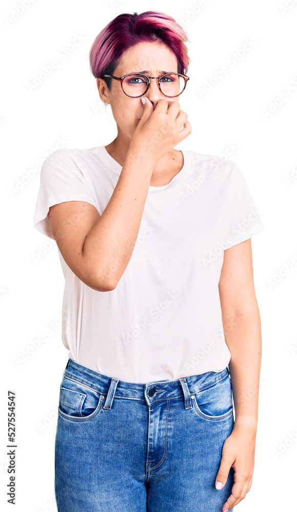 Young beautiful woman with pink hair wearing casual clothes and glasses smelling something stinky and disgusting, intolerable smell, holding breath with fingers on nose. bad smell Young beautiful woman with pink hair wearing casual clothes and glasses smelling something stinky and disgusting, intolerable smell, holding breath with fingers on nose. bad smell