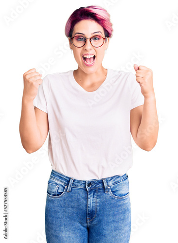 Young beautiful woman with pink hair wearing casual clothes and glasses celebrating surprised and amazed for success with arms raised and open eyes. winner concept.