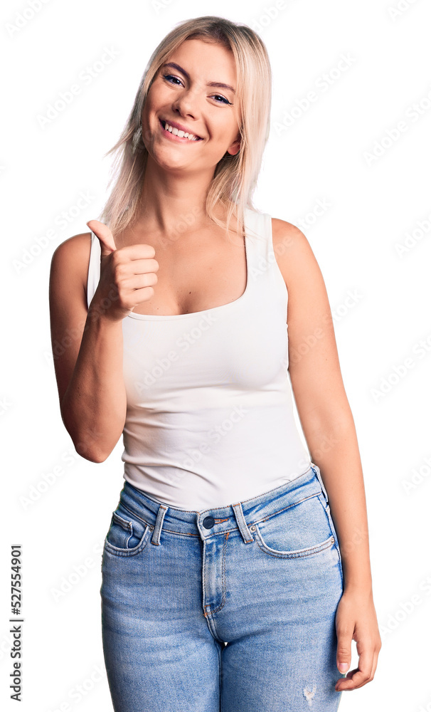 Young beautiful blonde woman wearing casual sleeveless t-shirt doing happy thumbs up gesture with hand. approving expression looking at the camera showing success. Young beautiful blonde woman wearing casual sleeveless t-shirt doing happy thumbs up gesture with hand. approving expression looking at the camera showing success.