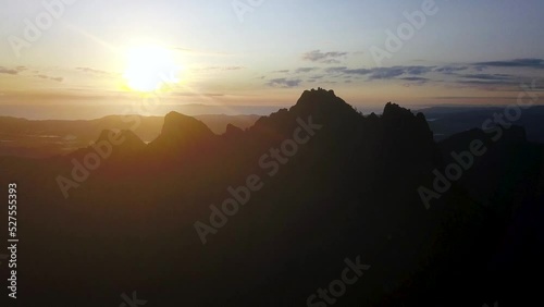 At dusk, a golden sunset and purple clouds set behind craggy mountain peaks in New Zealand. Ascending orbital drone shot. 