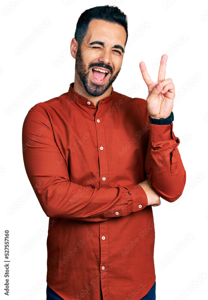 Young hispanic man with beard wearing casual shirt smiling with happy face winking at the camera doing victory sign with fingers. number two. Young hispanic man with beard wearing casual shirt smiling with happy face winking at the camera doing victory sign with fingers. number two.