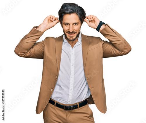 Young hispanic man wearing business clothes smiling pulling ears with fingers, funny gesture. audition problem