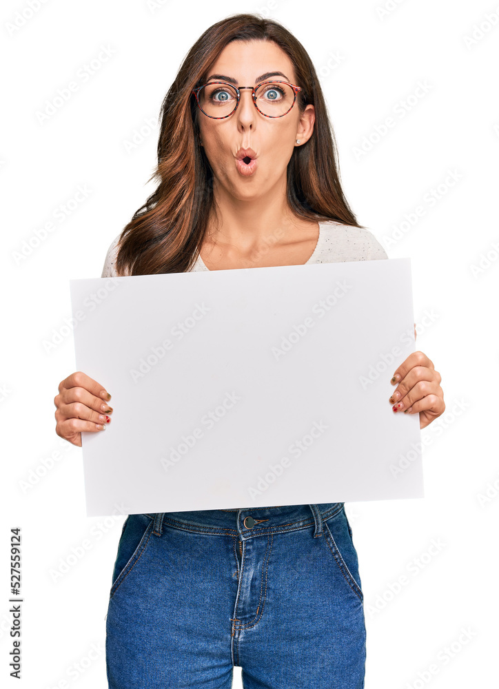 Young brunette woman holding blank empty banner scared and amazed with open mouth for surprise, disbelief face Young brunette woman holding blank empty banner scared and amazed with open mouth for surprise, disbelief face