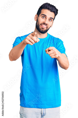 Young handsome man with beard wearing casual t-shirt pointing fingers to camera with happy and funny face. good energy and vibes.