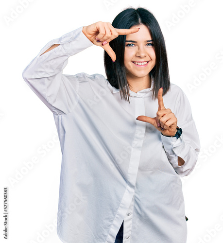 Young brunette woman with blue eyes wearing oversize white shirt smiling making frame with hands and fingers with happy face. creativity and photography concept.
