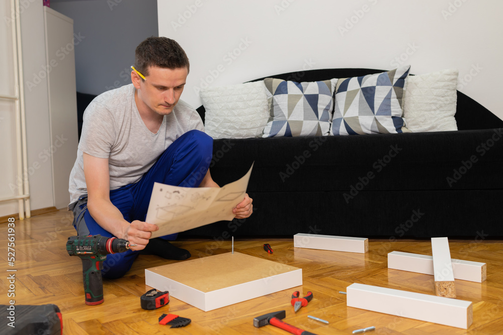Confused man assembling new wooden furniture at home. Man reading instructions and misunderstand what to do the next. Confused man assembling new wooden furniture at home. Man reading instructions and misunderstand what to do the next.