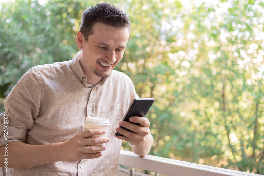 Young man using smartphone and drinking coffee outside. He is happy to exchange messages with friends, uses free internet connection on electronic modern gadget. Young man using smartphone and drinking coffee outside. He is happy to exchange messages with friends, uses free internet connection on electronic modern gadget.