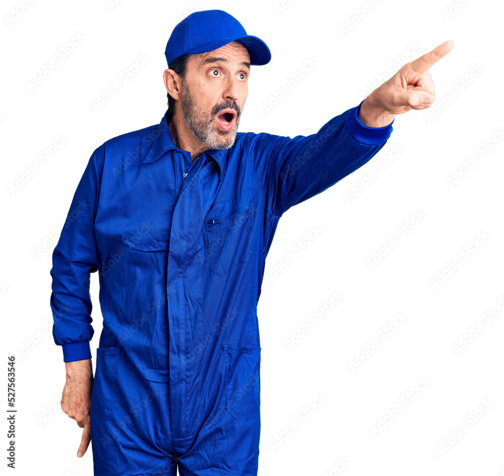Middle age handsome man wearing mechanic uniform pointing with finger surprised ahead, open mouth amazed expression, something on the front