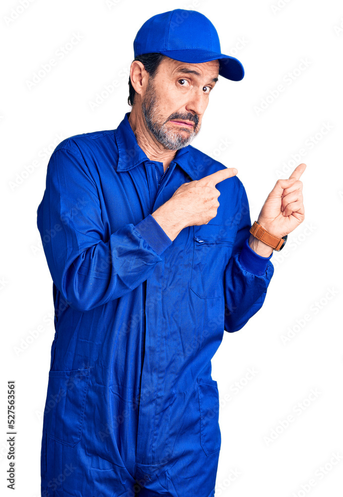 Middle age handsome man wearing mechanic uniform pointing aside worried and nervous with both hands, concerned and surprised expression Middle age handsome man wearing mechanic uniform pointing aside worried and nervous with both hands, concerned and surprised expression