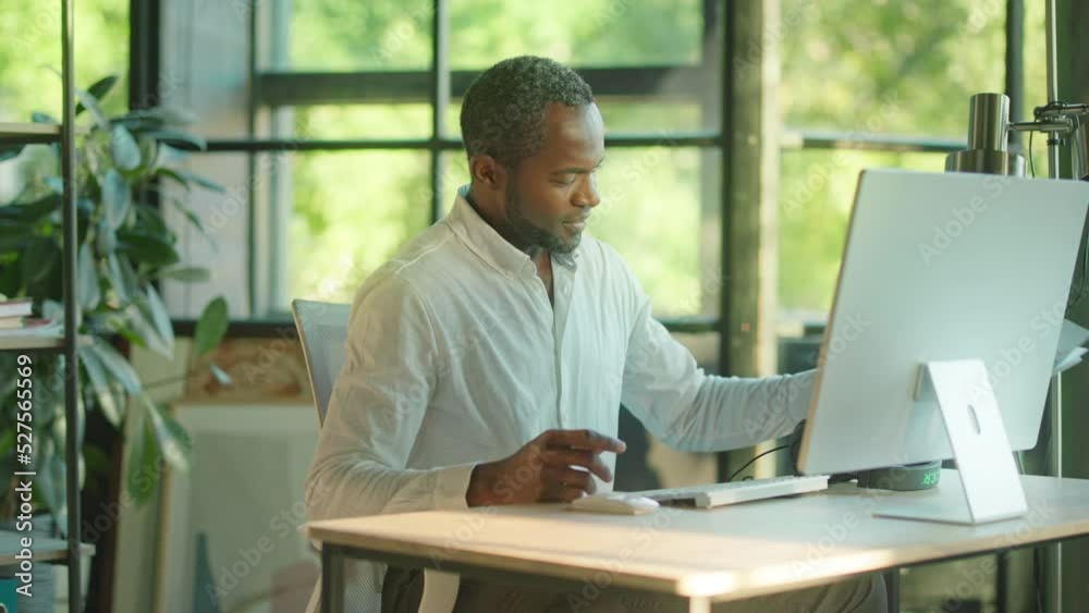 Close up attractive successful young african american man office worker holds paper after use computer and headphones smiling feel happy looking on screen in the office. Slow motion Close up attractive successful young african american man office worker holds paper after use computer and headphones smiling feel happy looking on screen in the office. Slow motion