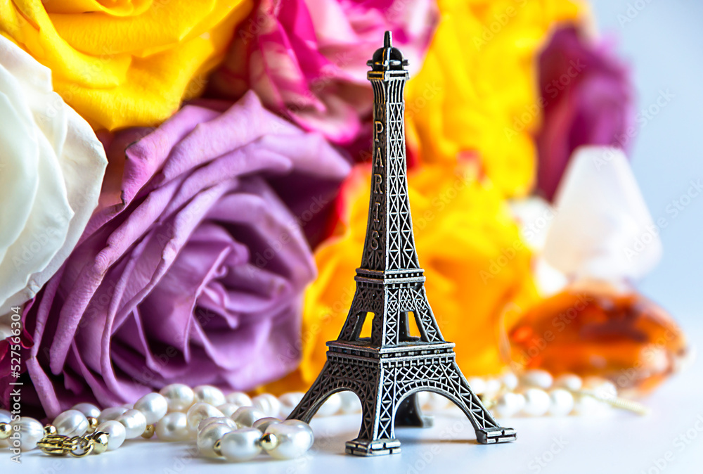 Miniature Eiffel Tower against the backdrop of a bouquet of roses, pearl jewelry and a bottle of perfume. The concept of female pleasures, holiday, travel, symbols