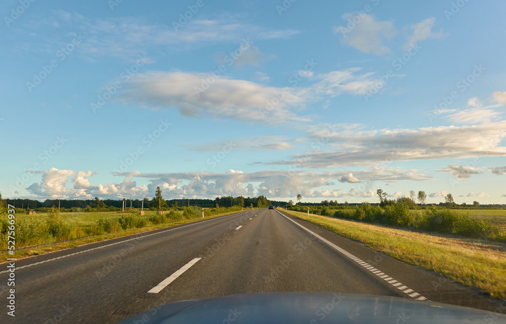 Highway (new asphalt road) through the agricultural field and forest at sunset. Dramatic sky after the thunderstorm. Summer, early autumn. Vacations, adventure, road trip, remote places. View from car