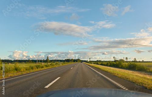 Highway (new asphalt road) through the agricultural field and forest at sunset. Dramatic sky after the thunderstorm. Summer, early autumn. Vacations, adventure, road trip, remote places. View from car