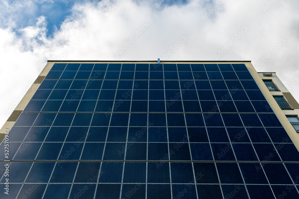 A modern energy-efficient building against the background of clouds. Multi-storey residential building with solar panels on the wall. Renewable energy sources in the city A modern energy-efficient building against the background of clouds. Multi-storey residential building with solar panels on the wall. Renewable energy sources in the city