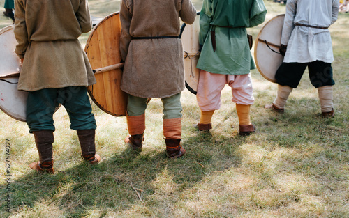 Back view of medieval soldiers with shields standing in a row on the grass on the battlefield. Cropped image
