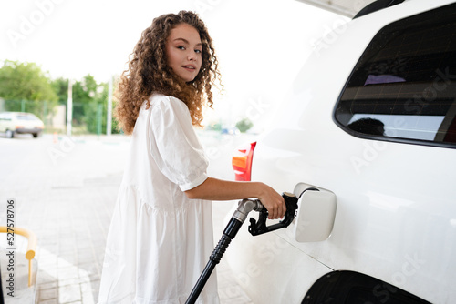 Young curly woman refueling car at gas station