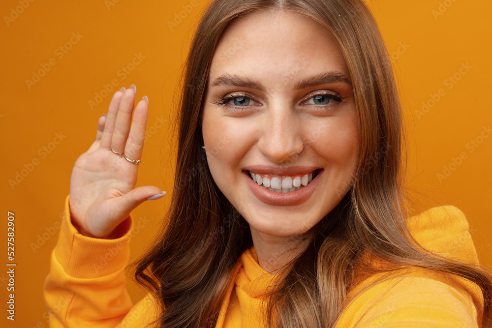 Happy cheerful woman with curly hair waving hello at smartphone camera on yellow background Happy cheerful woman with curly hair waving hello at smartphone camera on yellow background