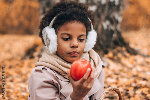 Cute African-American girl eats an apple at a picnic in an autumn park.Diversity,autumn concept.