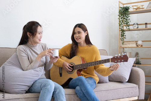 A young woman playing guitar on the sofa in the living room. Young Asian loving lovers couple bonding at home, relaxing on sofa the living room.