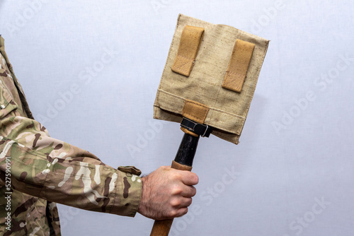 A sapper shovel in a case in the hand of a military man on a light background.