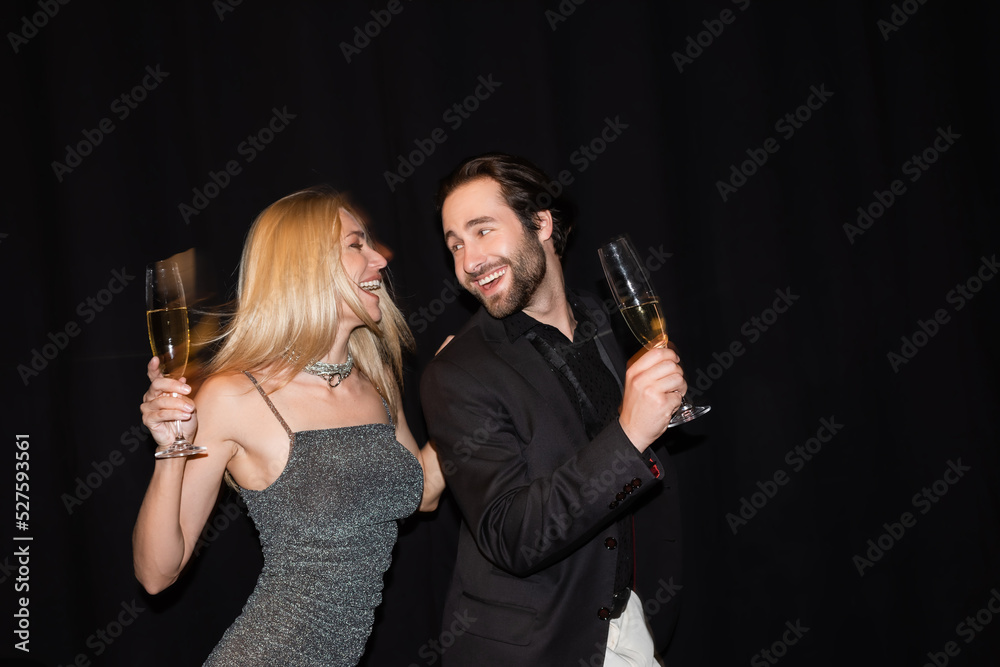 Motion blur of positive couple with champagne glasses during party isolated on black.