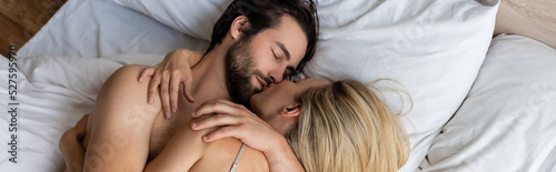 top view of brunette man and blonde woman hugging while lying on bed, banner.