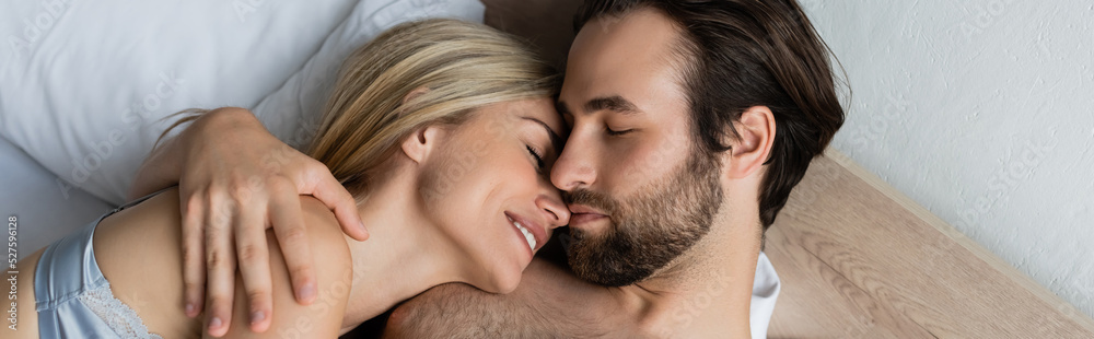 top view of brunette man hugging smiling woman while lying on bed with closed eyes, banner. top view of brunette man hugging smiling woman while lying on bed with closed eyes, banner.