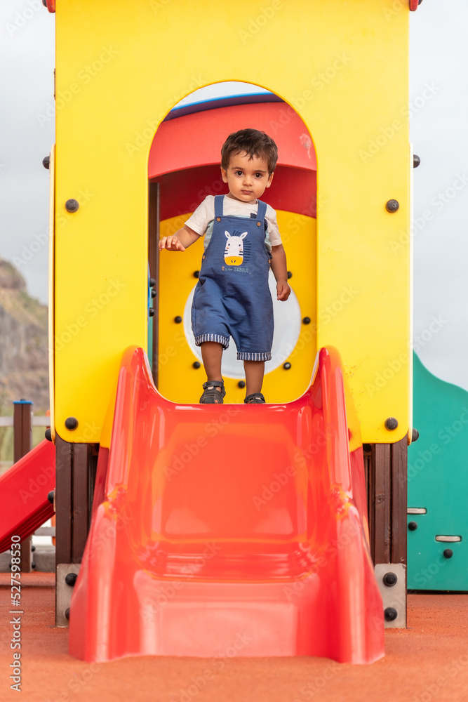 One year old boy playing in a playground having fun in summer, limited and controlled environment