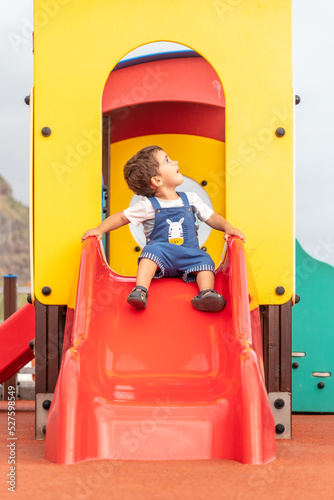 One year old boy playing in a playground having fun in summer, park adapted for babies