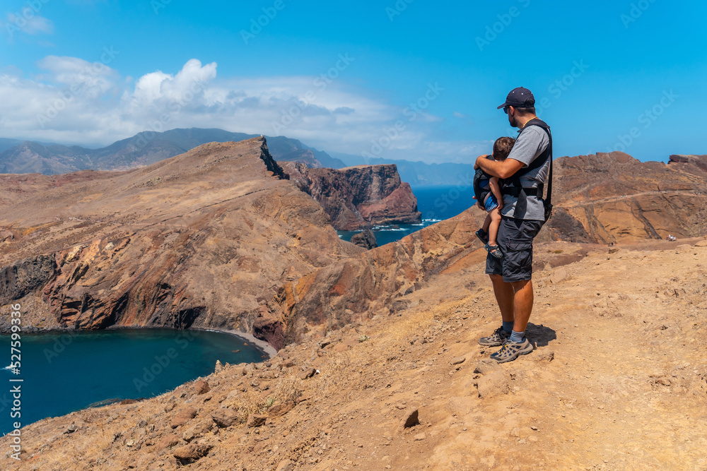 A father with his baby in his backpack in Ponta de Sao Lourenco looking at the landscape and the sea, Madeira
