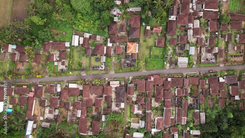 Panning aerial shot, plan view of common Balinese village. Many house compounds with separated buildings along central street. Red tiled roofs and some covered with modern materials Panning aerial shot, plan view of common Balinese village. Many house compounds with separated buildings along central street. Red tiled roofs and some covered with modern materials