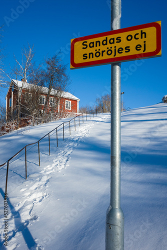 Winter in Sweden, Warning sign "Not sanded and cleared of snow", Fresh snow covered stairway on hill leading to traditional swedish red wooden house on top, sunny day, Vasteras Scandinavia