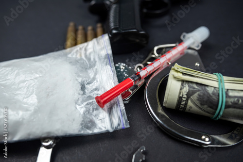 Drugs and money gun with silencer and handcuffs isolated on black table.
