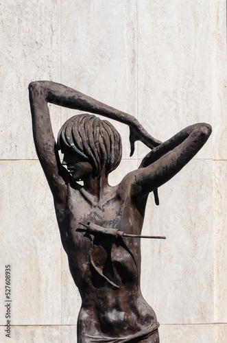 La statua bronzea di un ragazzo con le braccia alzate su una tomba del cimitero maggiore di Milano