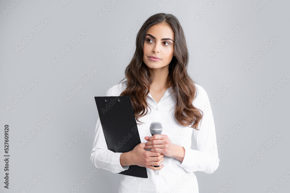 Portrait of young smiling business woman doing presentation with clipboard and microphone isolated grey background. Portrait of young smiling business woman doing presentation with clipboard and microphone isolated grey background.