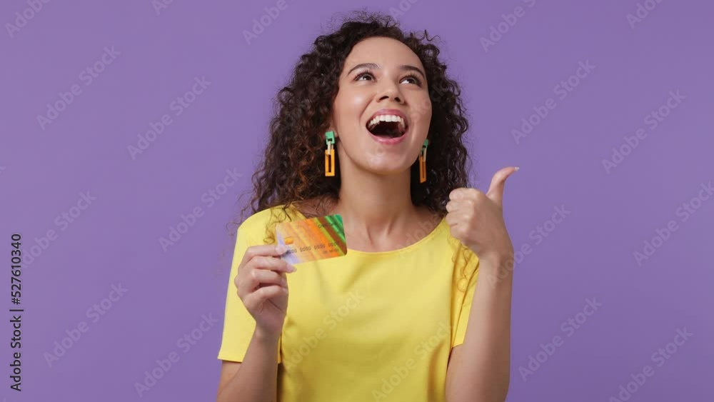 Young woman of African American ethnicity 20s she wear yellow t-shirt pointing index finger on mockup plastic credit bank card showing thumbs up isolated on plain pastel light purple background studio Young woman of African American ethnicity 20s she wear yellow t-shirt pointing index finger on mockup plastic credit bank card showing thumbs up isolated on plain pastel light purple background studio