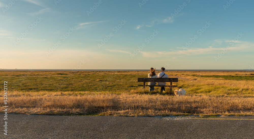 People (couple) sit on a bench in the middle of nowhere. Flat, remote, peaceful, meadow landscape. People (couple) sit on a bench in the middle of nowhere. Flat, remote, peaceful, meadow landscape.
