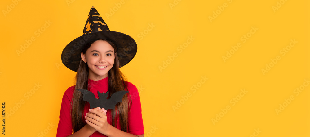 happy kid with bat wearing witch hat on yellow background, witchery. Halloween kid girl portrait, horizontal poster. Banner header with copy space.