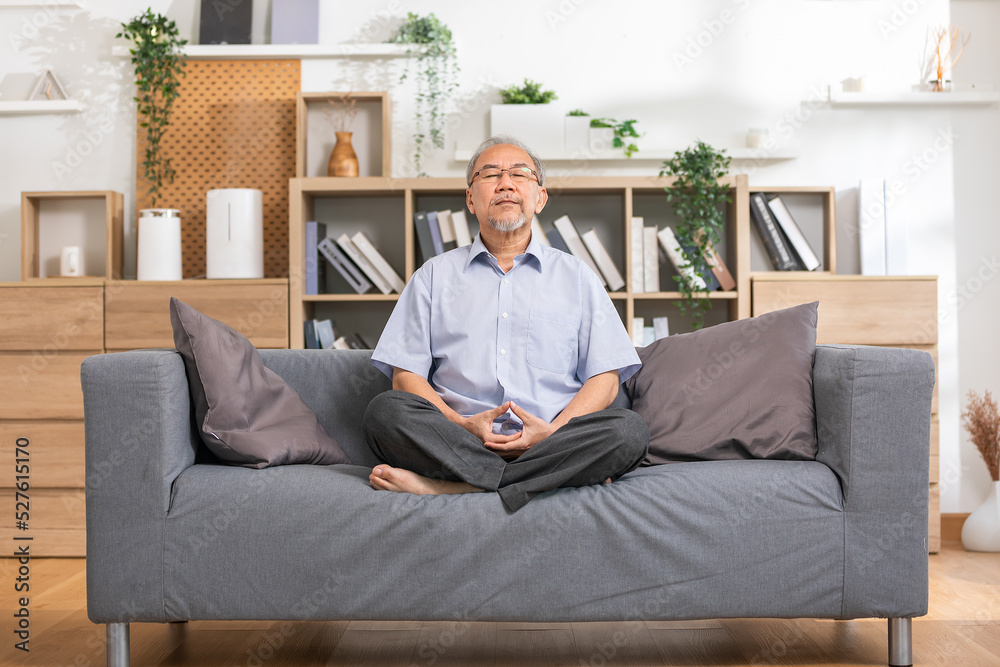Mature Asian man doing yoga for meditation on yoga mat in living room at home.Clam of senior or elderly men meditation deep breath and relax at cozy home.Happy Retired Meditation at home concept