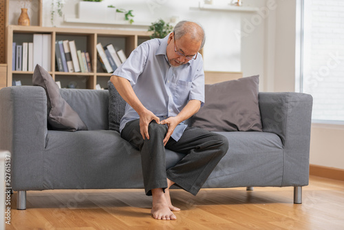 Asian old man with his knee joint pain in sofa, pain in the elderly, health care, elderly care. Elderly man having a knee pain and sitting down. Grandfather with knee pain.