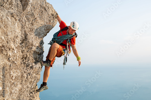 Foto Young male climber climbs a difficult route with a view of the sea at sunset