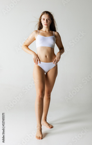 One young girl with long glossy hair wearing white underwear isolated over gray background. Wellness, wellbeing, aesthetic cosmetology concept.