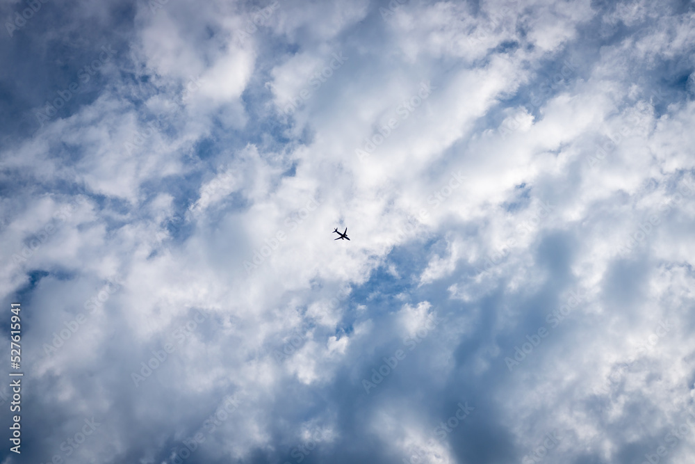 The plane on a background of the blue sky with clouds. Plane silhouette in the center of the photo frame