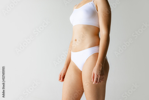 Close-up hips, belly, chest. Female tanned body of young woman in white underwear isolated on gray background. Natural beauty concept.