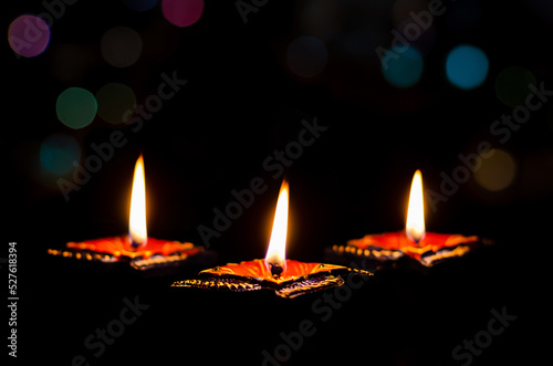 Selective focus on flame of first clay diya lamps lit on dark background with colorful bokeh lights. Diwali festival concept.