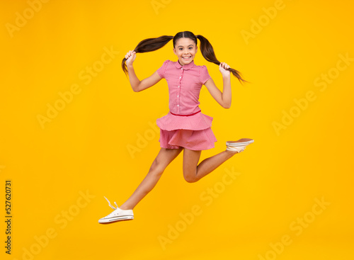 Fototapeta Naklejka Na Ścianę i Meble -  Excited teenager. Full length funny teenager kid jump enjoy rejoice win isolated on yellow background. Small child girl in dress jumping.
