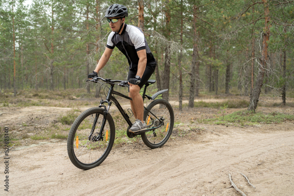 Active sport a man rides a mountain bike in a helmet and equipment on the road in a green forest