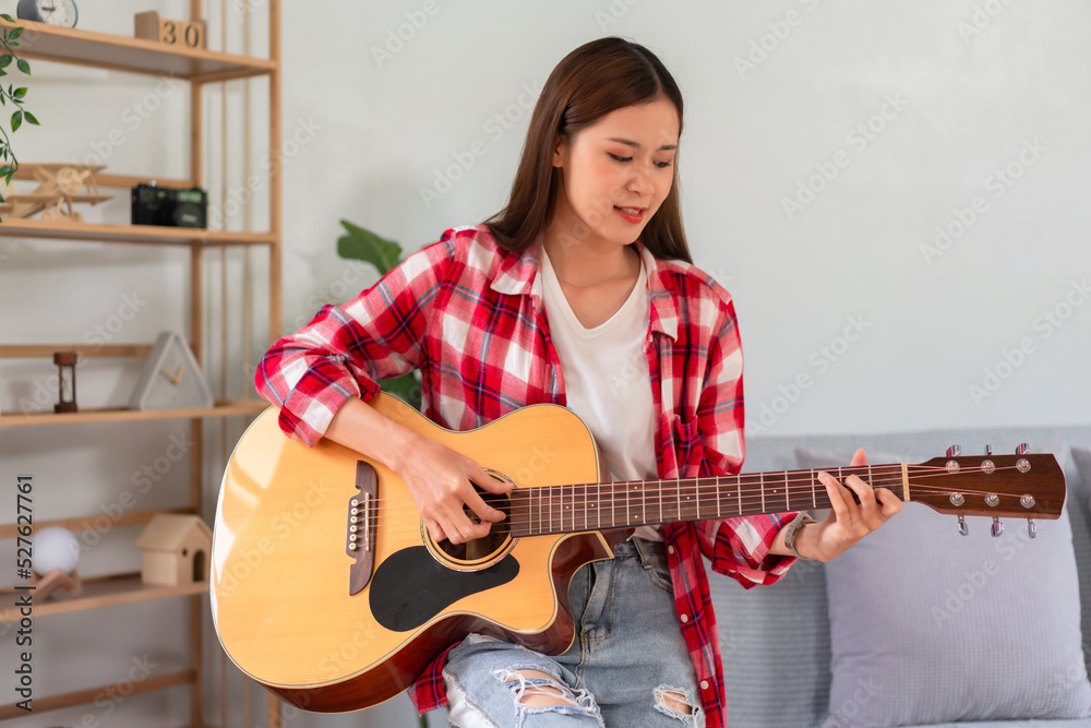 Fototapeta premium Hobby concept, Young asian woman learning and practice playing chords with acoustic guitar on couch