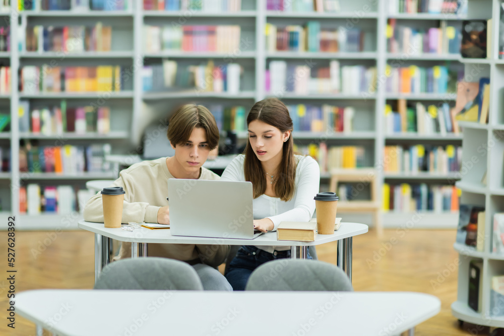 couple of teenagers studying near laptop and paper cups in library. couple of teenagers studying near laptop and paper cups in library.