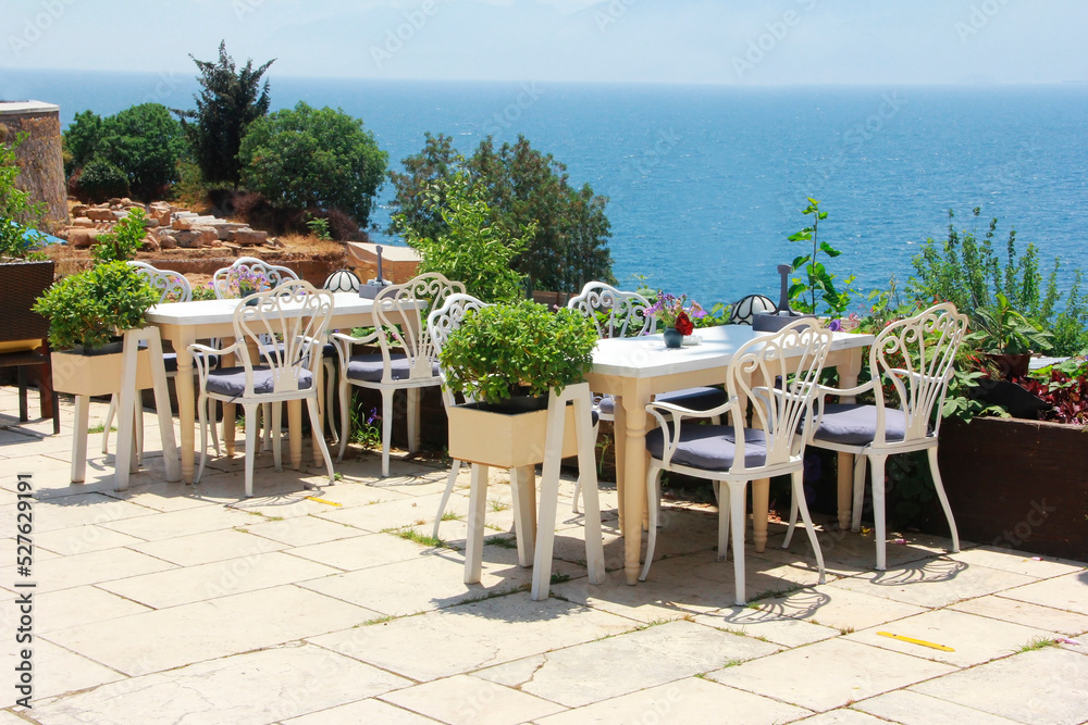 outdoor cafe with tables and chairs on the outdoor terrace overlooking the blue sea